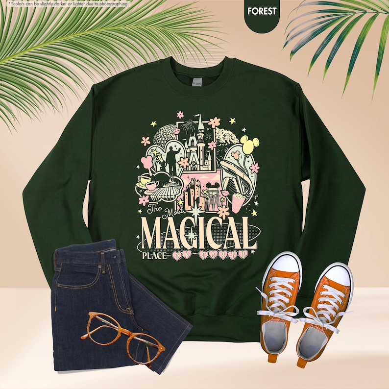 May include: Forest green sweatshirt with a colorful graphic that reads "The Most Magical Place." The graphic includes a castle, Mickey Mouse, and other theme park elements. Paired with blue jeans, orange sneakers, and glasses.
