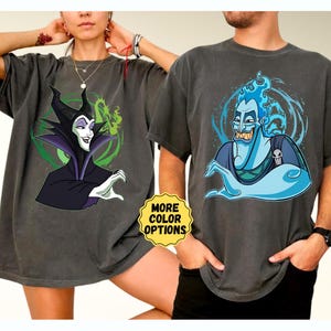 Puede incluir: Dos camisetas gris carb&oacute;n con gr&aacute;ficos de personajes de dibujos animados. Una camiseta muestra a Mal&eacute;fica con un fondo verde y negro. La otra camiseta muestra a Hades con llamas azules y una calavera. Una pegatina amarilla dice "MORE COLOR OPTIONS".