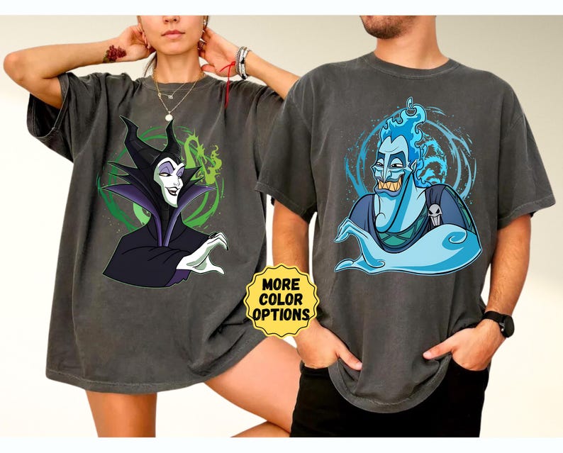 Puede incluir: Dos camisetas gris carb&oacute;n con gr&aacute;ficos de personajes de dibujos animados. Una camiseta muestra a Mal&eacute;fica con un fondo verde y negro. La otra camiseta muestra a Hades con llamas azules y una calavera. Una pegatina amarilla dice "MORE COLOR OPTIONS".
