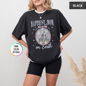 May include: Black t-shirt with the text "Happiest Mom on Earth" and a graphic of a castle inside a decorative oval. The design includes a pink bow, stars, and the words "on Earth".