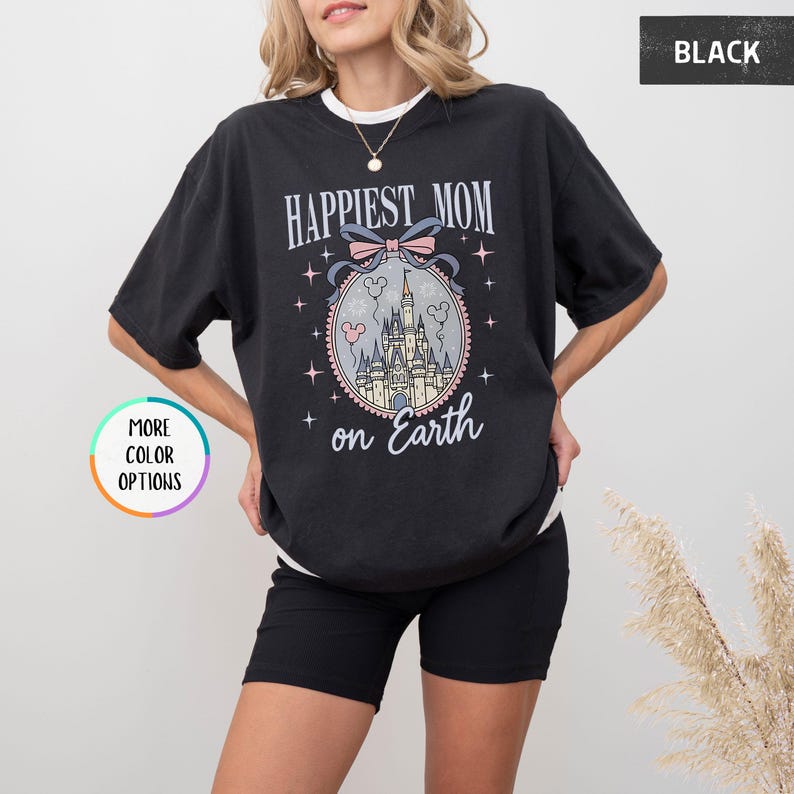 May include: Black t-shirt with the text "Happiest Mom on Earth" and a graphic of a castle inside a decorative oval. The design includes a pink bow, stars, and the words "on Earth".