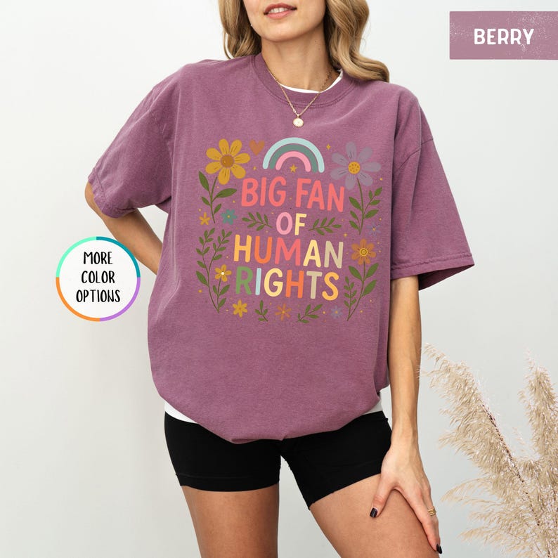 May include: Berry-colored t-shirt with the text "BIG FAN OF HUMAN RIGHTS" in colorful letters, surrounded by floral and rainbow graphics. The shirt is a relaxed fit and has short sleeves.