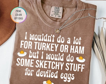 May include: Espresso-colored t-shirt with the text "I wouldn't do a lot FOR TURKEY OR HAM but I would do SOME SKETCHY STUFF for deviled eggs." The shirt has a crew neck and short sleeves. A silver necklace is draped across the shirt.