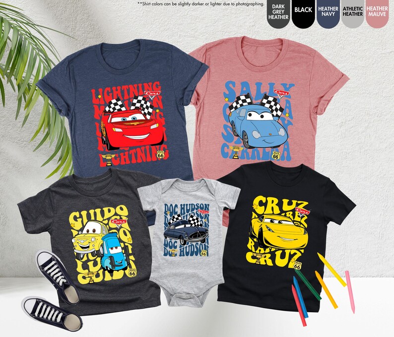 May include: A collection of t-shirts and a baby onesie with characters from the Cars movie. Designs feature Lightning McQueen, Sally Carrera, Guido, Doc Hudson, and Cruz Ramirez. Each item has a Route 66 graphic.
