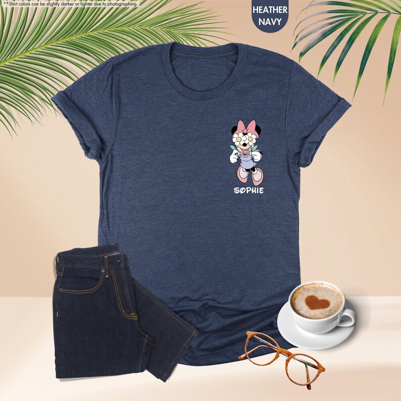 May include: Heather navy blue t-shirt with a Minnie Mouse graphic and the name "SOPHIE". The shirt is paired with dark blue jeans, a cup of coffee with a heart design, and eyeglasses. The shirt's color may vary slightly.
