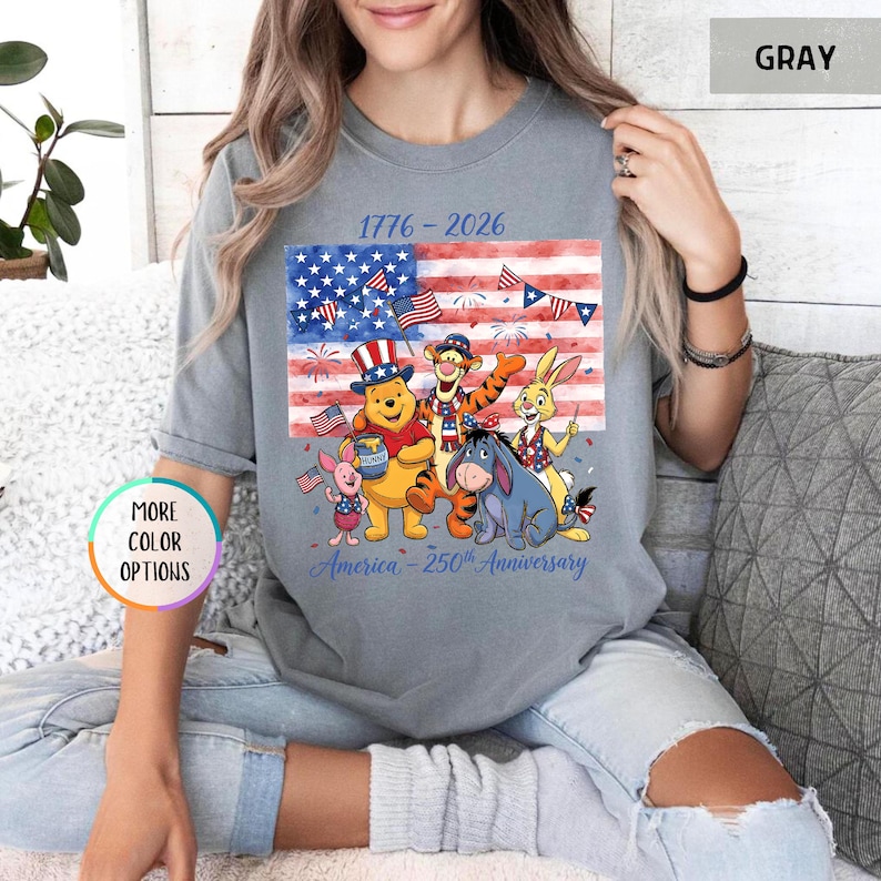 May include: Gray t-shirt featuring a patriotic design with the American flag and cartoon characters. The shirt has the text "1776-2026" and "America - 250th Anniversary". The design includes Winnie the Pooh, Tigger, Eeyore, and Rabbit.