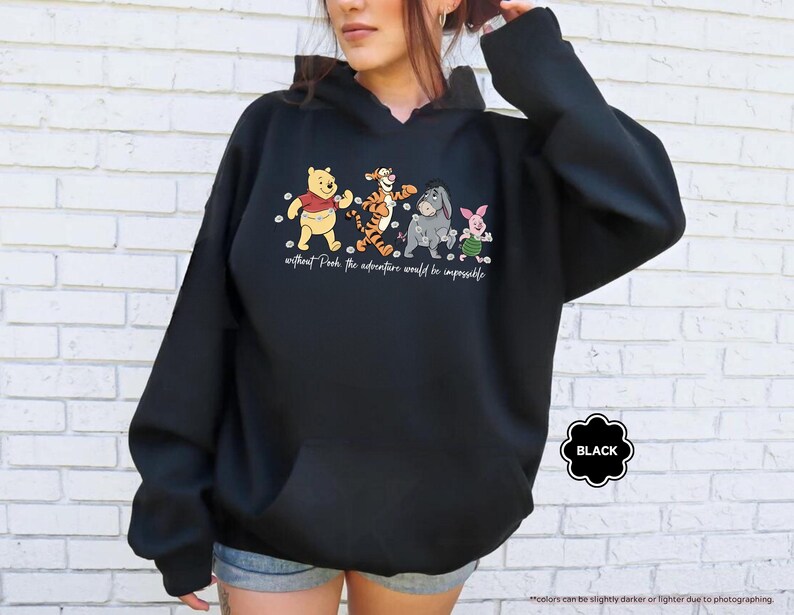 Puede incluir: Sudadera con capucha negra con un gr&aacute;fico de Winnie the Pooh, Tigger, Eeyore y Piglet. El texto "without Pooh the adventure would be impossible" est&aacute; impreso debajo de los personajes. Una etiqueta negra est&aacute; en la esquina inferior derecha.