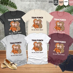 May include: A collection of t-shirts in various colors, each featuring a graphic of two hugging monkeys and the text "TEAM PUNCH" and "You are never alone!". Colors include heather grey, white, peach, mauve, and dark heather.