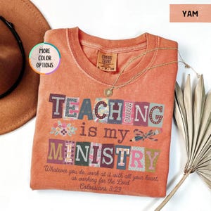 Pu&ograve; includere: Una maglietta color igname con le parole "TEACHING is my MINISTRY" in lettere a blocchi colorate. La maglietta include il versetto biblico Colossesi 3:23. Sono visibili anche una collana d'oro e un cappello marrone.