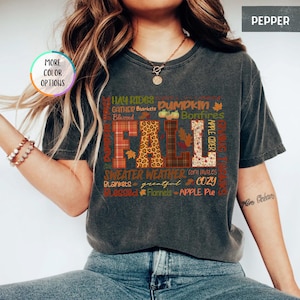 以下が含まれることがあります： チェック柄やヒョウ柄など、さまざまな模様と色で「FALL」という文字がプリントされた濃いグレーのTシャツ。Tシャツには、「Pumpkin」、「Bonfires」、「Sweater Weather」などの秋をテーマにした言葉も含まれています。