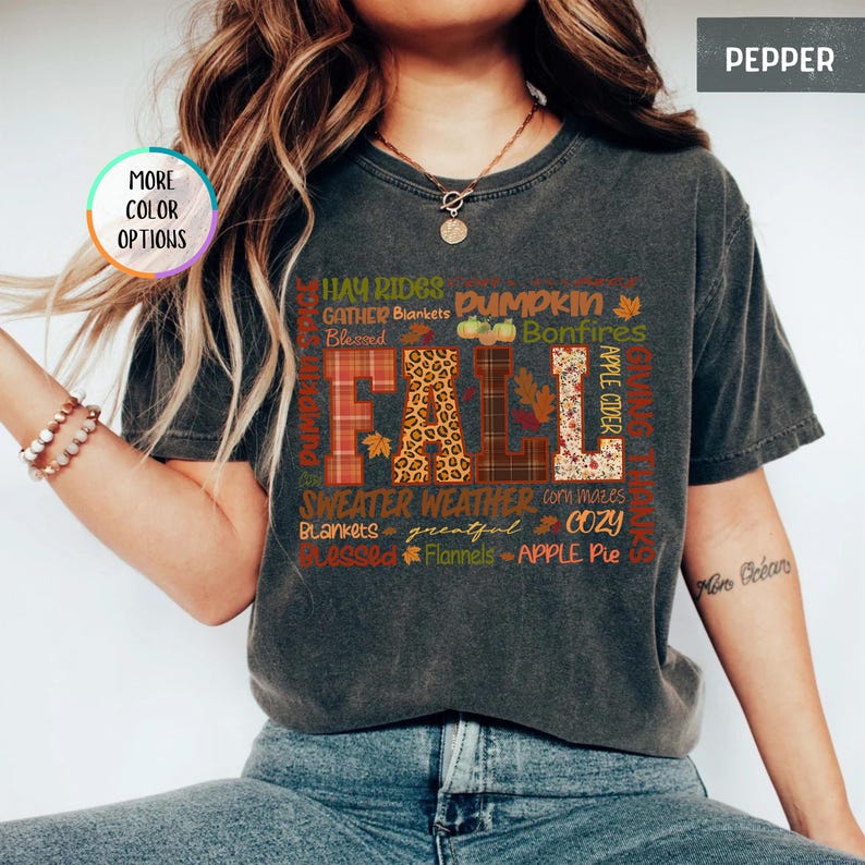 以下が含まれることがあります： チェック柄やヒョウ柄など、さまざまな模様と色で「FALL」という文字がプリントされた濃いグレーのTシャツ。Tシャツには、「Pumpkin」、「Bonfires」、「Sweater Weather」などの秋をテーマにした言葉も含まれています。