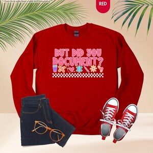 Puede incluir: Una sudadera roja con el texto "BUT DID YOU DOCUMENT?" en rosa y blanco, con gr&aacute;ficos de tem&aacute;tica m&eacute;dica. La imagen tambi&eacute;n muestra unos vaqueros azules, gafas con montura dorada y zapatillas rojas.