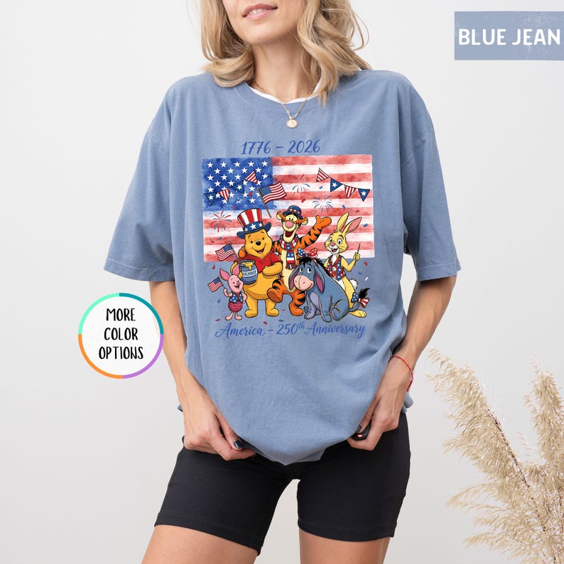 May include: Blue jean colored t-shirt featuring a graphic of the American flag with fireworks and cartoon characters. The text on the shirt reads "1776-2026" and "America - 250th Anniversary".
