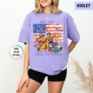 May include: Violet t-shirt featuring a graphic of Winnie the Pooh and friends celebrating the 250th anniversary of America. The design includes an American flag and the text "1776-2026" and "America - 250th Anniversary".