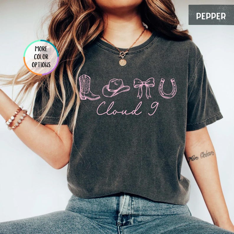 May include: A dark gray t-shirt with a pink graphic featuring a cowboy boot, hat, bow, and horseshoe, with the words "Cloud 9" in a script font. The shirt has a vintage, worn look.