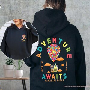 Puede incluir: Sudadera con capucha negra con un gr&aacute;fico colorido en la espalda que dice "Adventure Awaits Paradise Falls" con un dise&ntilde;o de casa y globo. La parte delantera de la sudadera tiene una versi&oacute;n m&aacute;s peque&ntilde;a del gr&aacute;fico. La sudadera tiene una capucha con cord&oacute;n.