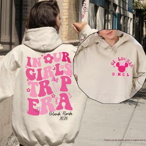 Peut inclure: Sweat &agrave; capuche couleur sable avec le texte rose "IN OUR GIRLS TRIP ERA" et "Orlando, Florida 2026" en dessous. Le devant du sweat &agrave; capuche pr&eacute;sente un motif Minnie Mouse et le texte "GIRLS TRIP DNEL".