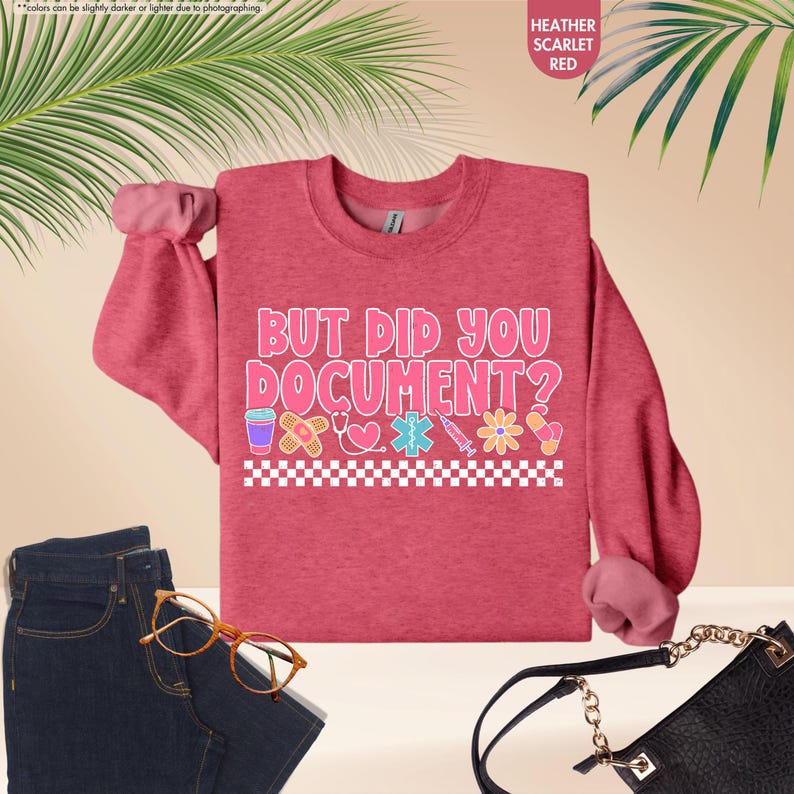 Puede incluir: Sudadera roja escarlata jaspeada con el texto "BUT DID YOU DOCUMENT?" en rosa y blanco. El dise&ntilde;o incluye iconos m&eacute;dicos. La imagen tambi&eacute;n muestra unos vaqueros azules y un bolso negro.