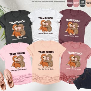 May include: A collection of t-shirts in various colors, including heather gray, white, and pink. Each shirt features the text "TEAM PUNCH" above an illustration of two hugging monkeys, with the phrase "You are never alone!" below.