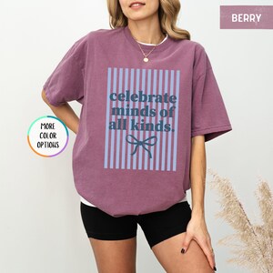 Puede incluir: Camiseta color bayas con el texto "celebrate minds of all kinds" en un dise&ntilde;o de rayas azules y blancas. La camiseta tiene un corte holgado y mangas cortas. La modelo lleva shorts negros.