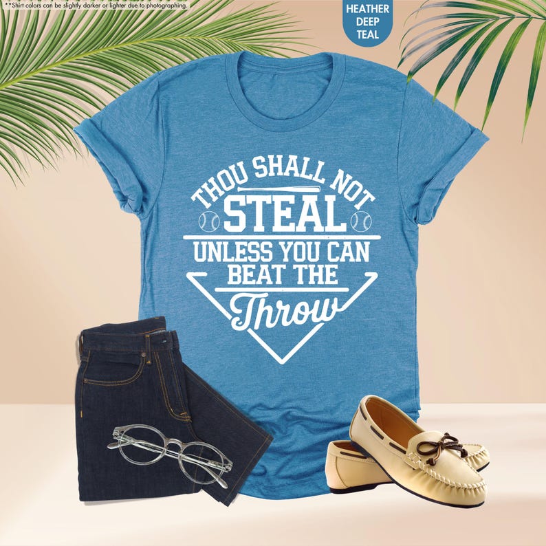 May include: A teal t-shirt with the text "THOU SHALL NOT STEAL UNLESS YOU CAN BEAT THE THROW" in white, paired with dark blue jeans, clear-framed glasses, and cream-colored loafers with brown bows. The shirt is heather deep teal.