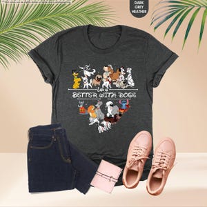 May include: Dark grey heather t-shirt with a heart-shaped graphic of cartoon dogs and the text "Life is Better With Dogs." The shirt is paired with blue jeans, a pink wallet, and pink sneakers.