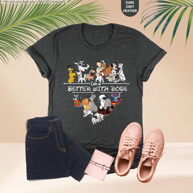 May include: Dark grey heather t-shirt with a heart-shaped graphic of cartoon dogs and the text "Life is Better With Dogs." The shirt is paired with blue jeans, a pink wallet, and pink sneakers.