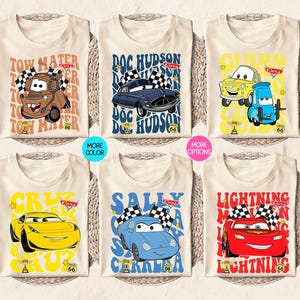 以下が含まれることがあります： 6枚のベージュ色のTシャツ。それぞれ、カーズのキャラクター、メーター、ドック・ハドソン、ライトニング・マックィーンなどのカラフルな漫画の車のグラフィックがプリントされています。テキストとレーシングフラッグも含まれています。