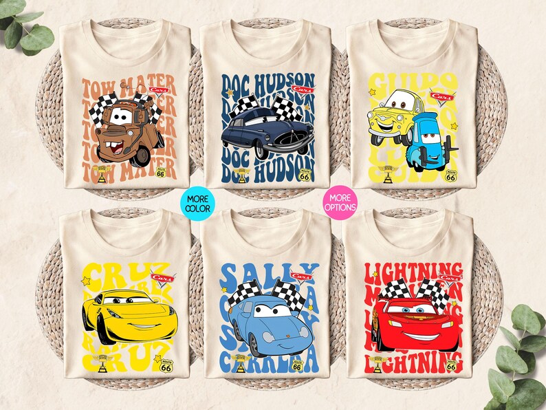 以下が含まれることがあります： 6枚のベージュ色のTシャツ。それぞれ、カーズのキャラクター、メーター、ドック・ハドソン、ライトニング・マックィーンなどのカラフルな漫画の車のグラフィックがプリントされています。テキストとレーシングフラッグも含まれています。