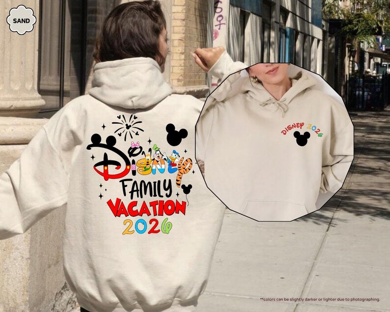 Puede incluir: Una sudadera con capucha color arena que presenta un gr&aacute;fico grande en la espalda con el texto Disney Family Vacation 2026, orejas de Mickey Mouse, fuegos artificiales y personajes. El pecho muestra un peque&ntilde;o icono de Mickey Mouse y Disney 2026.
