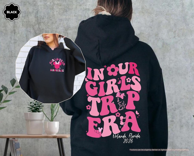 Peut inclure: Sweat &agrave; capuche noir avec un motif rose au dos indiquant "IN OUR GIRLS TRIP ERA" avec un design Minnie Mouse et le texte "Orlando, Florida 2026". L'avant du sweat &agrave; capuche porte un motif plus petit avec "GIRLS TRIP" et "DANIELLE".