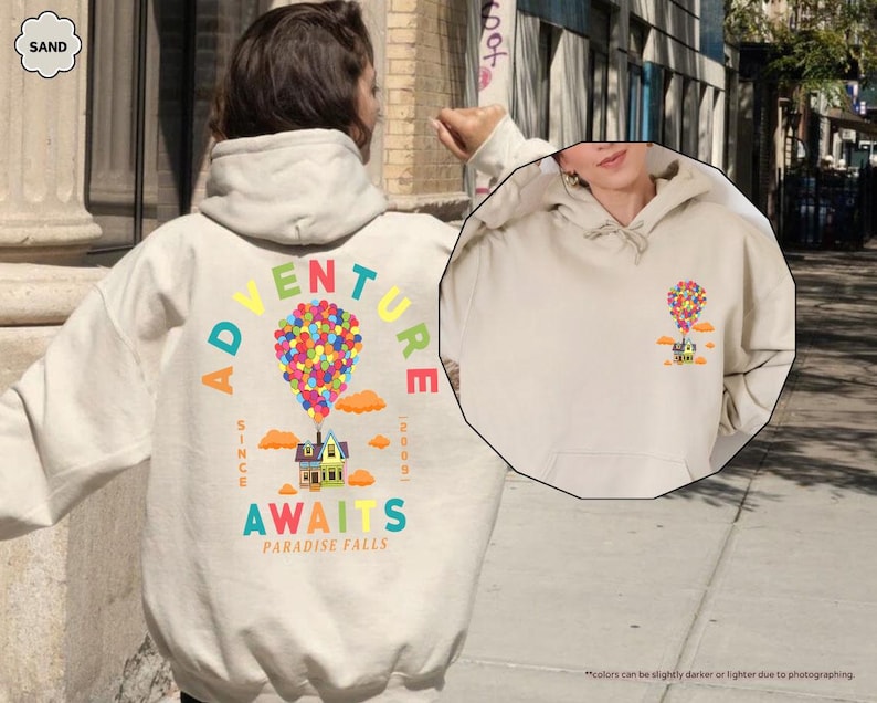 Puede incluir: Sudadera con capucha de color arena con un gr&aacute;fico colorido de una casa levantada por globos. El texto "ADVENTURE AWAITS PARADISE FALLS" est&aacute; impreso en la parte posterior. La sudadera tiene un bolsillo delantero y una capucha.