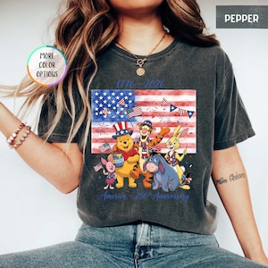 May include: Dark gray t-shirt featuring a graphic of Winnie the Pooh and friends in front of an American flag. The shirt has the text "1776-2026" and "America - 250th Anniversary".