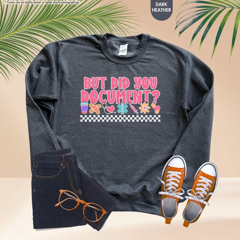 Puede incluir: Sudadera gris oscuro con el texto "BUT DID YOU DOCUMENT?" en rosa y blanco. El dise&ntilde;o incluye gr&aacute;ficos de tem&aacute;tica m&eacute;dica. La imagen tambi&eacute;n muestra unos vaqueros, zapatillas naranjas y gafas.