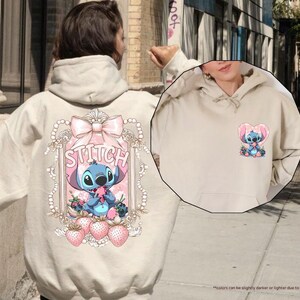 Puede incluir: Sudadera con capucha color arena con un gr&aacute;fico de Stitch en la espalda y una versi&oacute;n m&aacute;s peque&ntilde;a en la parte delantera. El dise&ntilde;o de la espalda incluye un lazo rosa, la palabra "Stitch" y fresas. La sudadera tiene una capucha con cord&oacute;n.