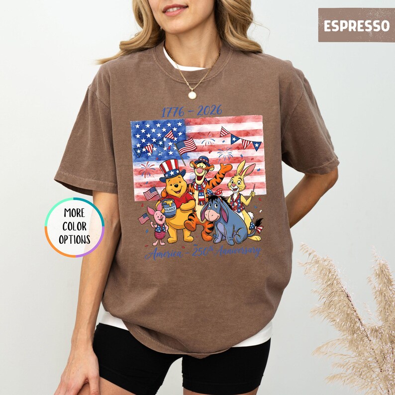May include: Espresso-colored t-shirt featuring a graphic of Winnie the Pooh and friends in front of an American flag. The shirt has the text "1776-2026" and "America 250th Anniversary". The shirt has a round neck and short sleeves.
