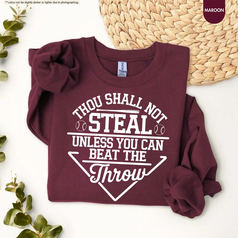 May include: Maroon sweatshirt with the text "THOU SHALL NOT STEAL UNLESS YOU CAN BEAT THE THROW" in white. The design includes baseballs and a baseball diamond shape. The sweatshirt is a crew neck.