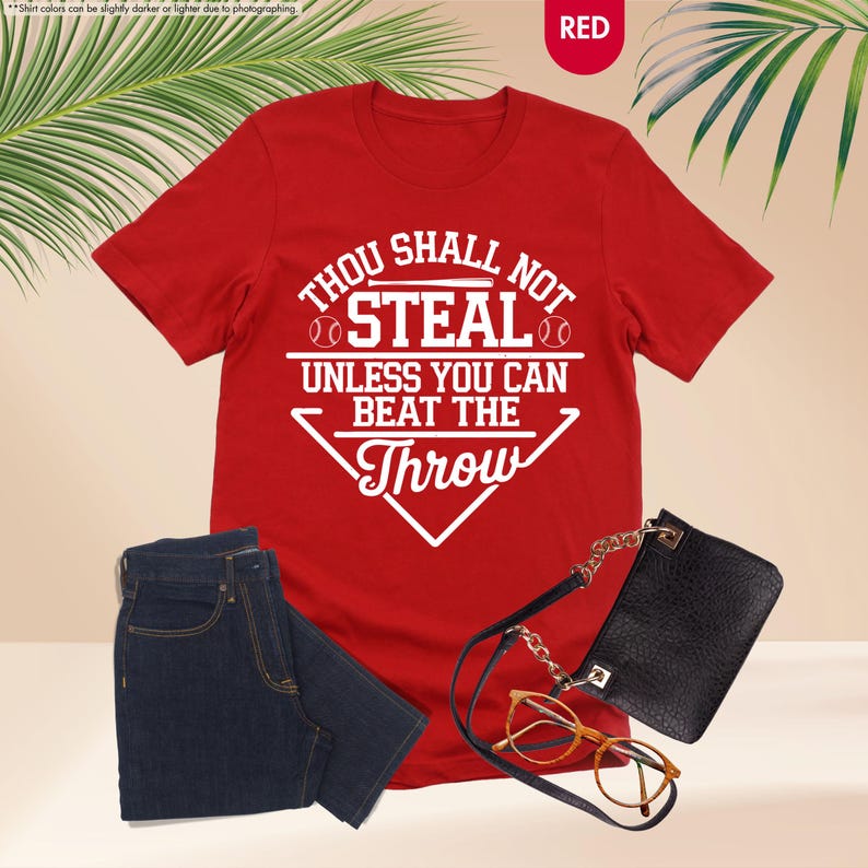 May include: A red t-shirt with the text "THOU SHALL NOT STEAL UNLESS YOU CAN BEAT THE THROW" in white. The image also shows a pair of dark blue jeans, a black purse, and eyeglasses.