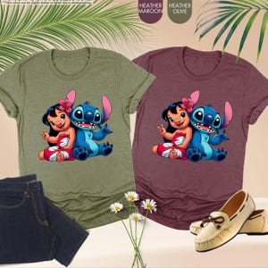 Puede incluir: Dos camisetas jaspeadas, una verde oliva y otra granate, con un dibujo animado de Lilo y Stitch. La camiseta verde oliva se combina con vaqueros oscuros. La camiseta granate se combina con mocasines color crema.