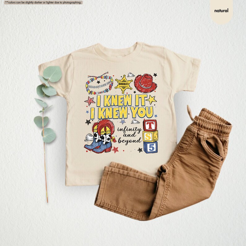 Peut inclure: Un t-shirt de couleur naturelle avec une impression graphique portant le texte I KNEW IT I KNEW YOU infinity and beyond. Le motif comprend un insigne de sh&eacute;rif, un chapeau de cow-boy rouge, des bottes de cow-boy et des blocs alphabet T, S, 5.