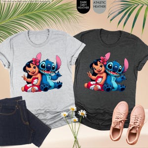 Puede incluir: Dos camisetas, una gris claro y otra gris oscuro, cada una con una imagen de dibujos animados de Lilo y Stitch. Las camisetas se muestran con un par de vaqueros azul oscuro y zapatillas rosas. El texto de la imagen dice "DARK GREY HEATHER" y "ATHLETIC HEATHER."