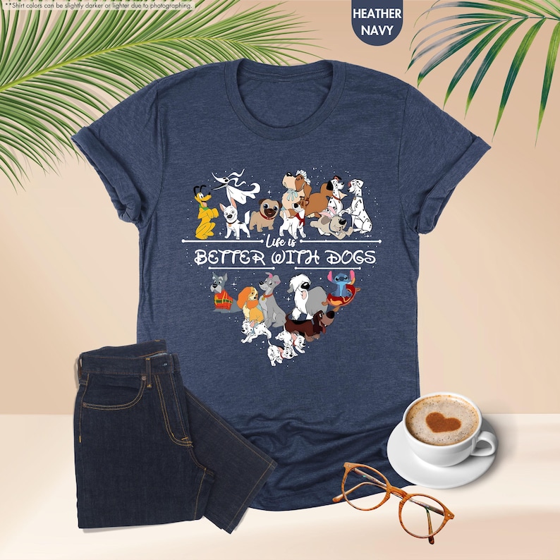 May include: Heather navy blue t-shirt with a graphic of various cartoon dogs arranged in a heart shape. The text "Life is Better With Dogs" is printed below the dogs. A pair of dark blue jeans, a cup of coffee, and glasses are also in the image.