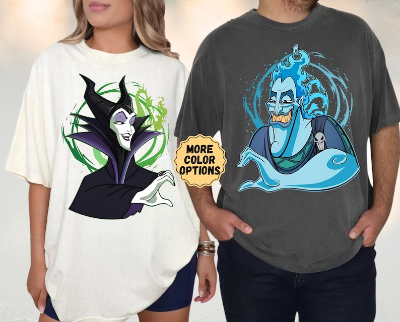 Puede incluir: Dos camisetas de gran tama&ntilde;o, una color crema y otra gris carb&oacute;n. La camiseta crema presenta una imagen de dibujos animados de Mal&eacute;fica, mientras que la camiseta gris muestra a Hades. Ambas camisetas tienen el texto "MORE COLOR OPTIONS" en una pegatina amarilla.