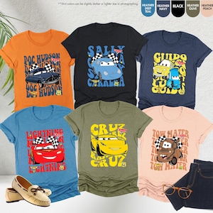 以下が含まれることがあります： 様々な色の半袖Tシャツのコレクションで、それぞれに漫画の車のデザインとテキストが描かれています。シャツの色はオレンジ、黒、ネイビー、オリーブ、ピーチ、ティールです。デザインには、映画「カーズ」のキャラクターとテキストが含まれています。