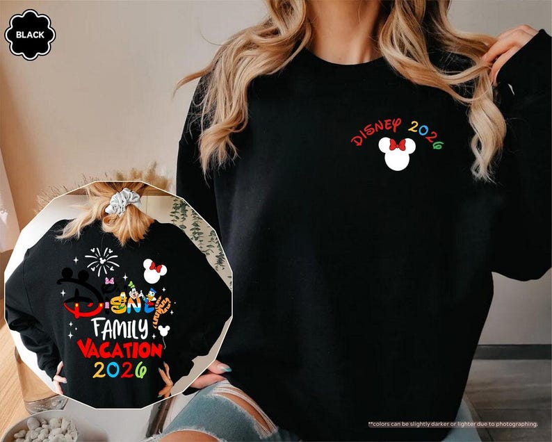 Puede incluir: Una sudadera negra de manga larga con un peque&ntilde;o icono blanco de la cabeza de Mickey Mouse con un lazo rojo, el texto DISNEY 2026 y un gr&aacute;fico grande en la espalda con personajes de Disney, fuegos artificiales y el texto DISNEY FAMILY VACATION 2026.