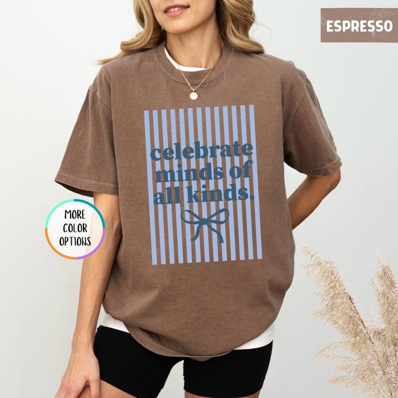 Puede incluir: Camiseta color espresso con el texto "celebrate minds of all kinds" en azul. El dise&ntilde;o incluye rayas verticales azules y un lazo. La camiseta es de estilo casual.