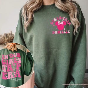 Peut inclure: Sweat-shirt vert militaire avec un motif rose sur le devant indiquant "GIRLS TRIP" avec un n&oelig;ud Minnie Mouse et le nom "DANIELLE". Le dos du sweat-shirt porte l'inscription "IN YOUR GIRLS TRIP ERA" et "Orlando, Florida 2026".