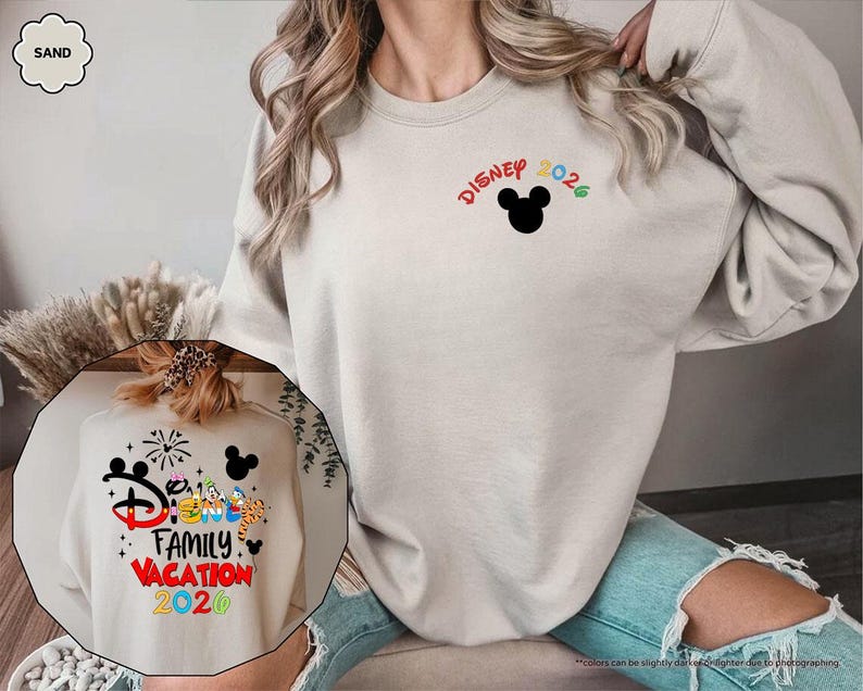 Puede incluir: Una sudadera de cuello redondo color arena que presenta una peque&ntilde;a silueta negra de Mickey Mouse con el texto Disney 2026 en el frente. El dise&ntilde;o posterior muestra el texto Disney Family Vacation 2026 con gr&aacute;ficos de personajes coloridos y fuegos artificiales.
