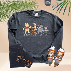 Puede incluir: Sudadera gris oscuro con un gr&aacute;fico de Winnie the Pooh, Tigger, Eeyore y Piglet. El texto "without Pooh the adventure would be impossible" est&aacute; debajo. La sudadera se muestra con vaqueros azules y zapatillas naranjas.