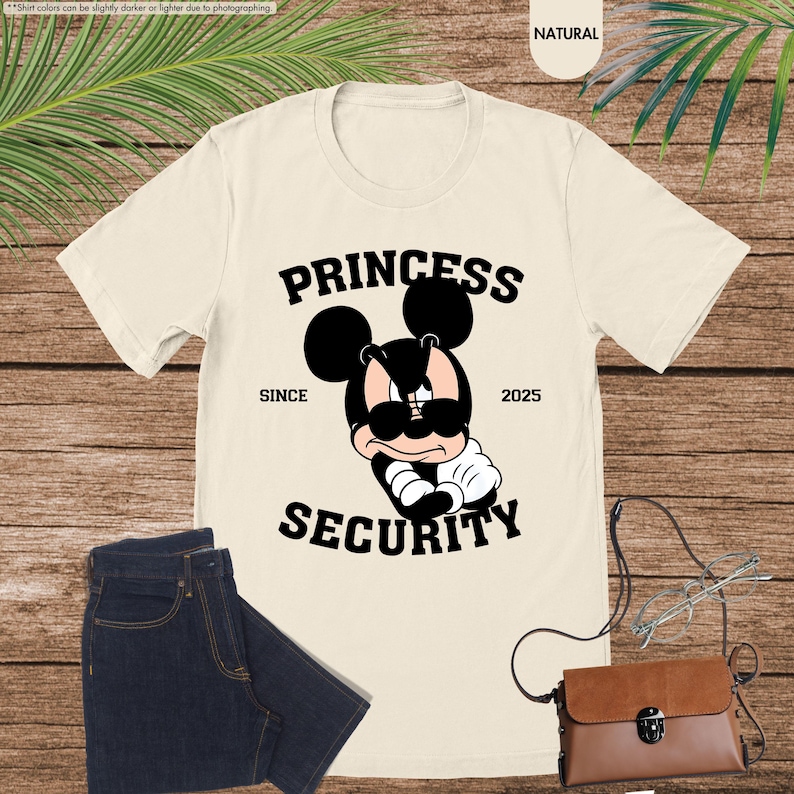 May include: A beige t-shirt with a black graphic of Mickey Mouse wearing sunglasses and the text "Princess Security" with "Since 2025" underneath.